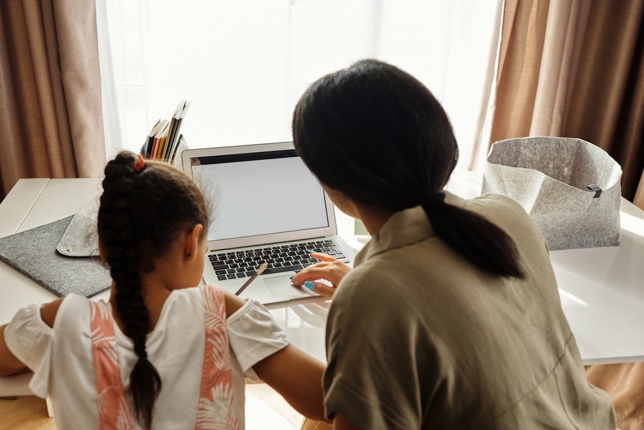 Services A mother helps her daughter with online learning on a laptop at home, emphasizing family education.