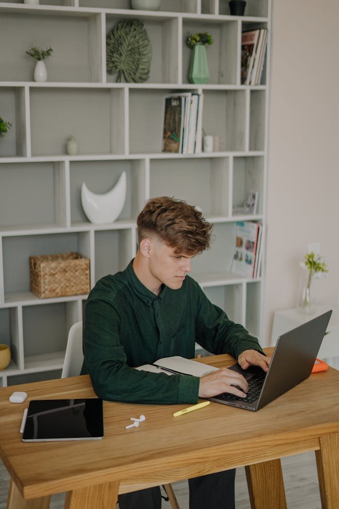 Services Adult man using laptop for online class at home. Modern technology setup on wooden desk.