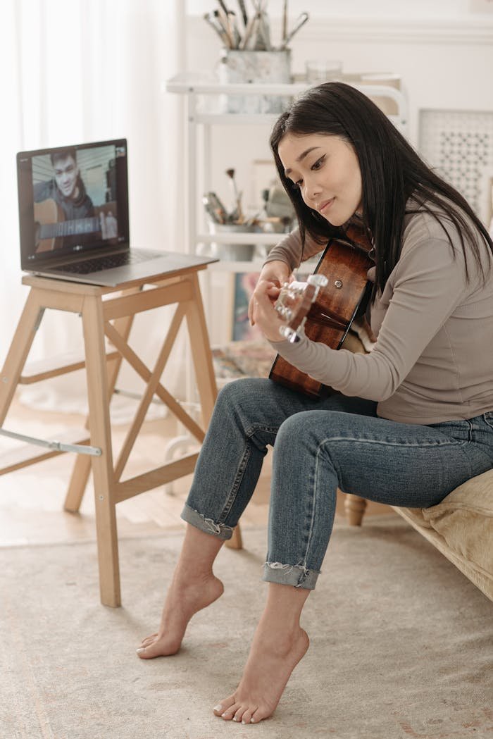 Woman learning guitar through an online class, sitting at home during the daytime.